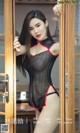 A woman in a black and red lingerie posing in front of a door.