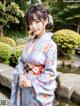 A woman in a blue kimono standing next to a pond.