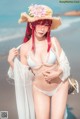 A woman in a white bikini and a straw hat on the beach.