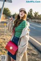 A woman in a striped shirt and trench coat holding a red bag.