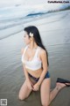 A woman in a white top and blue shorts sitting on the beach.