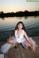 A woman in a white dress sitting on a dock by the water.