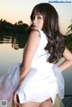 A woman in a white dress posing by a lake.