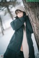 A woman leaning against a tree in the snow.