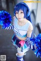 A woman in a cheerleading uniform holding blue pom poms.