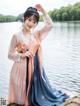 A woman in a blue and pink hanbok posing by the water.