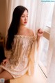 A woman sitting on a window sill in a white dress.