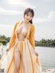 A woman in a yellow and white dress posing by the water.