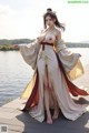 A woman in a long dress standing on a dock by the water.